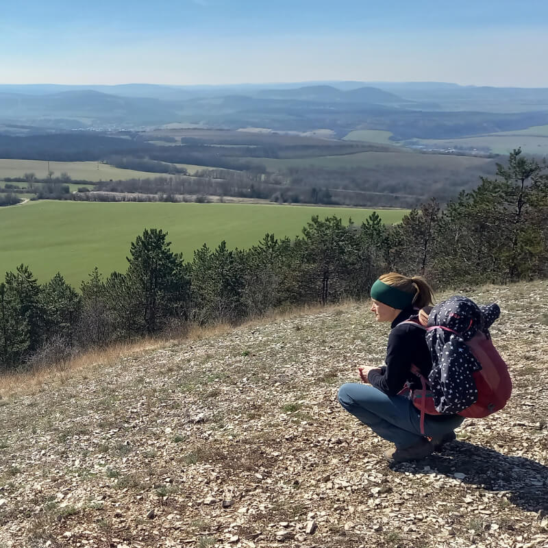 Egy turista guggolva nézi a tájat egy hegytetőről.