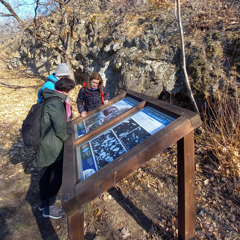 Turisták egy ismertető táblát olvasnak az andezitbánya bemutatóhelynél.